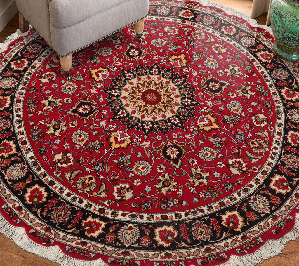 Round red, black patterned oriental area rug on a wooden floor with a chair partially visible.
