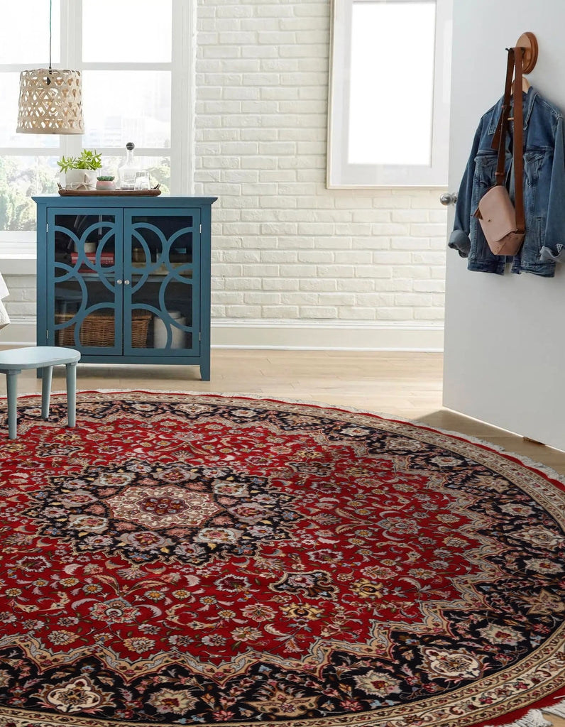 Round red and black patterned rug in a room with a blue cabinet and white walls.
